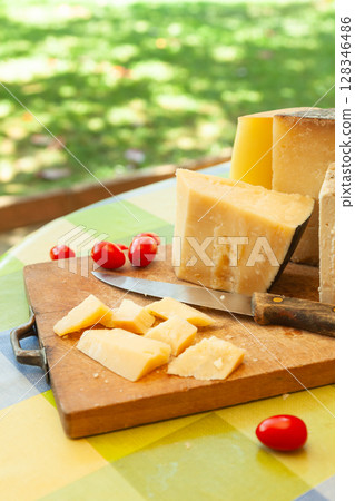 Chunky pieces of hard cheese with knife and cherry tomatoes on wooden board in bright outdoor setting Chunky pieces of hard cheese with knife and cherry tomatoes on wooden board in bright outdoor setting 128346486