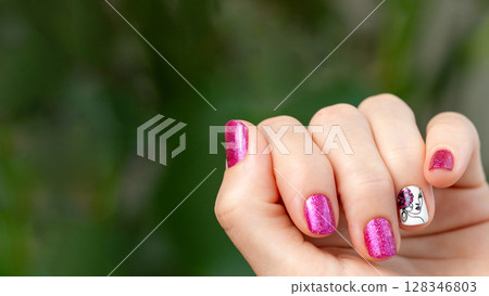 Female hand with pink manicure. Woman fingernails with pink holographic nail polish lacquer on green lush background. Aesthetic visual of red violet manicure with lady silhouette stamping. Copy space 128346803