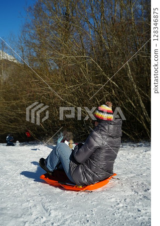 Person Sledding Down Snowy Hill on Bright Winter Day Person Sledding Down Snowy Hill on Bright Winter Day 128346875