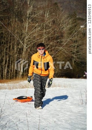 Teen Sledding on Snowy Day with Orange Sled 128346913
