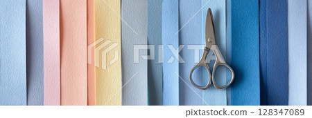 Colorful assortment of textured paper strips in pastel shades arranged neatly with a pair of silver scissors placed centrally, ideal for crafting and creative projects 128347089