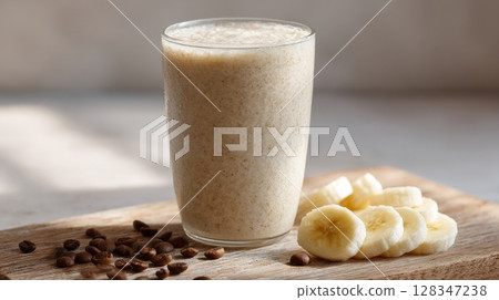 Creamy banana coffee smoothie in a glass, surrounded by fresh banana slices and coffee beans on a wooden board 128347238