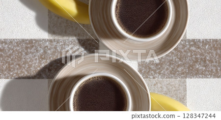 Two elegant coffee cups placed on a textured surface beside ripe bananas, showcasing a delightful morning beverage experience 128347244