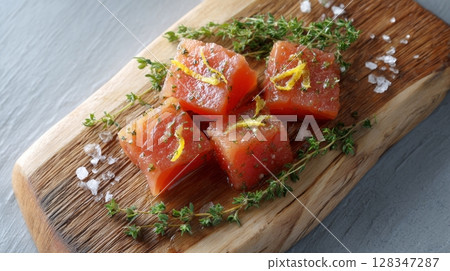 Candied salmon pieces garnished with fresh herbs and lemon zest on a rustic wooden board, showcasing vibrant colors and appetizing presentation 128347287