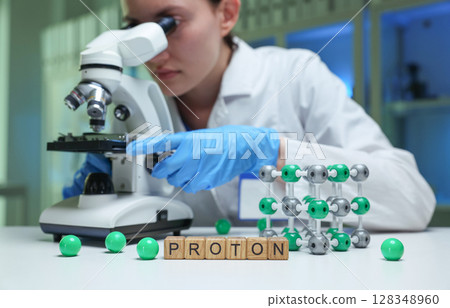 A scientist observing protons through a microscope in a lab for research and discovery A scientist observing protons through a microscope in a lab for research and discovery 128348960