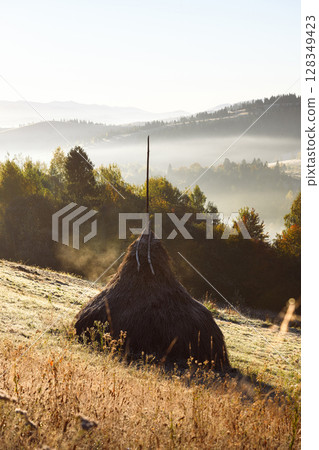 Haystack rest in foggy mountain field with warm sunrise 128349423