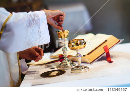 Priest draws consecrated host in wine for Eucharist Priest draws consecrated host in wine for Eucharist 128349567