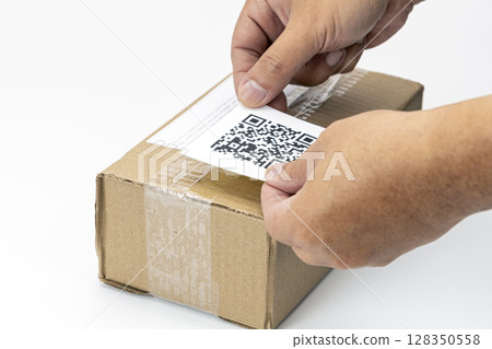 Hands placing QR code label on cardboard shipping box, symbolizing modern logistics and efficient package tracking. scene highlights integration of technology in shipping processes 128350558