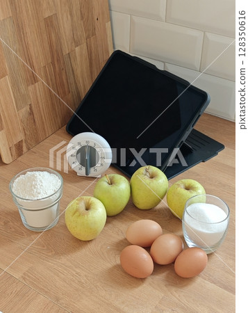 Fresh ingredients and kitchen tools arranged for baking adventures featuring apples, eggs, and sugar 128350616