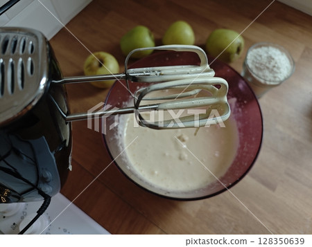 Mixing creamy batter while preparing a delicious dessert with fresh apples in a cozy kitchen setting Mixing creamy batter while preparing a delicious dessert with fresh apples in a cozy kitchen setting 128350639
