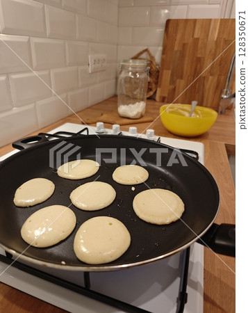 Fluffy pancakes cooking on a stovetop in a cozy kitchen during a morning breakfast preparation 128350671