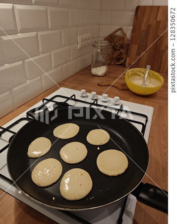 Cooking fluffy pancakes in a cozy kitchen during a weekend brunch with friends and family enjoying the warmth of home 128350672