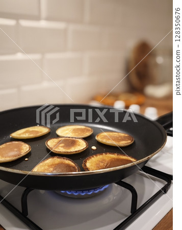 Fluffy golden pancakes cooking on a modern stovetop in a cozy kitchen atmosphere Fluffy golden pancakes cooking on a modern stovetop in a cozy kitchen atmosphere 128350676