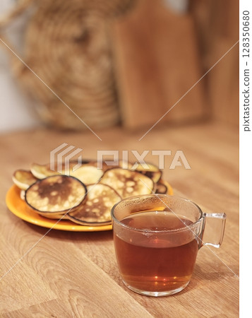 Delightful breakfast setting with steaming tea and golden pancakes on a rustic wooden table 128350680