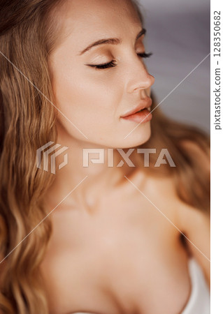 Sensual portrait of a sexy blonde young woman in a white off-the-shoulder dress. 128350682