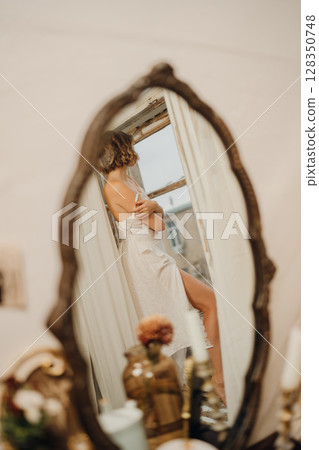 in the mirror of a beautiful young woman with blonde hair in a white dress 128350748