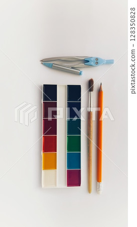 School supplies flat lay with watercolor paints, compass, pencil and brush on white background. Creative tools for drawing and learning. Back to school and artistic education concept. School supplies flat lay with watercolor paints, compass, pencil and brush on white background. Creative tools for drawing and learning. Back to school and artistic education concept. 128350828