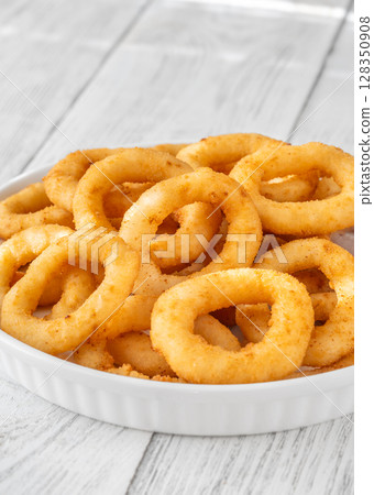 Golden onion rings stacked on plate atop white rustic wooden surface Golden onion rings stacked on plate atop white rustic wooden surface 128350908