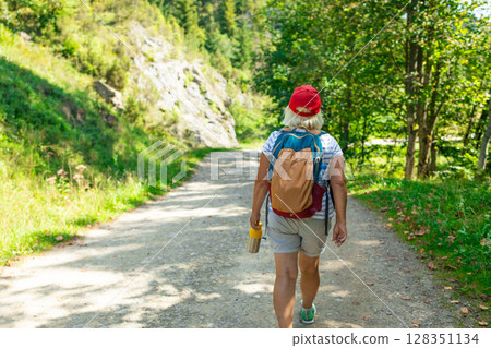 Senior Woman Walking on Forest Trail with Backpack Senior Woman Walking on Forest Trail with Backpack 128351134