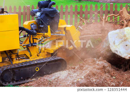 Powerful stump grinder works diligently in yard, removing an stump creating space for landscaping. Powerful stump grinder works diligently in yard, removing an stump creating space for landscaping. 128351444