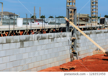 Workers are constructing masonry wall at construction site with materials arranged for ongoing building efforts. Workers are constructing masonry wall at construction site with materials arranged for ongoing building efforts. 128351450