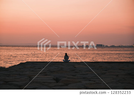 [Sennan Marble Beach] People watching the sunset on the beach illuminated by the beautiful light of the setting sun 128352233