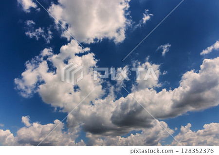 Puffy clouds drift across bright blue sky, creating calm peaceful atmosphere during sunny day. 128352376
