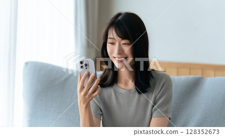 微笑的女人坐在沙發上使用智慧型手機 128352673