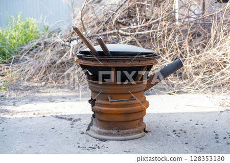Steel kazan, a large cast iron cauldron, on a fire pit for cooking outdoors. Outdoor cooking concept with wood burning stove 128353180
