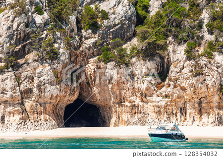 Boat anchored near sea cave entrance in rocky cliffs of Cala Luna beach on Sardinian eastern coast Boat anchored near sea cave entrance in rocky cliffs of Cala Luna beach on Sardinian eastern coast 128354032