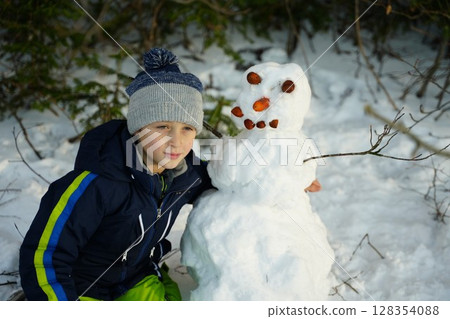 Young Boy Building a Snowman in Winter Wonderland 128354088