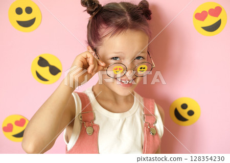 Funny girl with glasses on pink studio background with various emoticons depicting different emotions. world Smile and Emoji Day 128354230