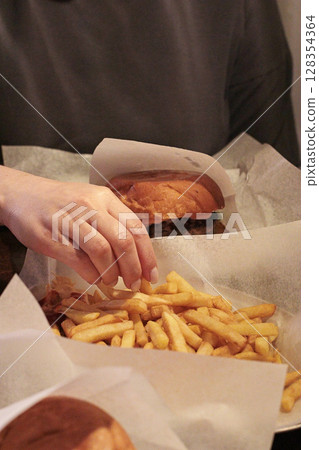 Urban lunch break moment with a person taking french fries from a paper tray at a cozy cafe. Relaxing dining scene, ideal for fast food, lifestyle, travel, or outdoor snack time visuals 128354364