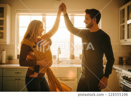 Couple enjoys a joyful dance in their kitchen during golden hour with baby in a sling 128355106
