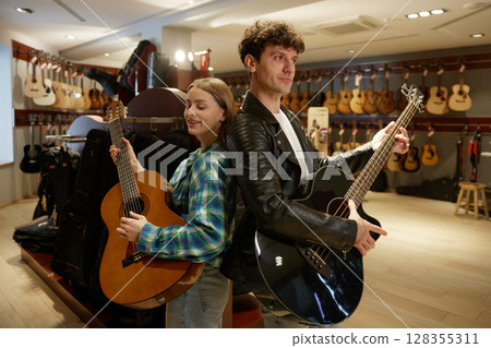 In a music store, a man and a woman are playing their guitars skillfully 128355311