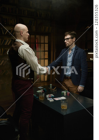 Two skilled players finalize an deal at poker table surrounded by colorful chips and cards 128355326