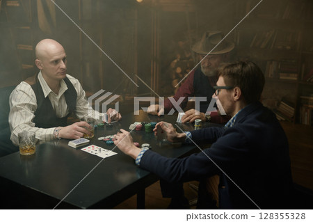 Three gentlemen playing poker game in a vintage old library Three gentlemen playing poker game in a vintage old library 128355328