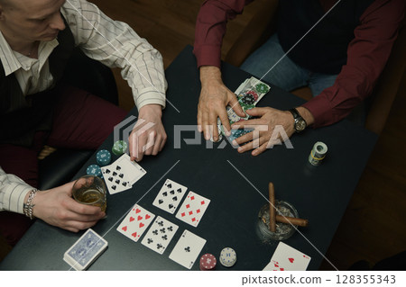 Thrilling moment at poker table with chips, stylish watch, and drink in dimly lit setting 128355343