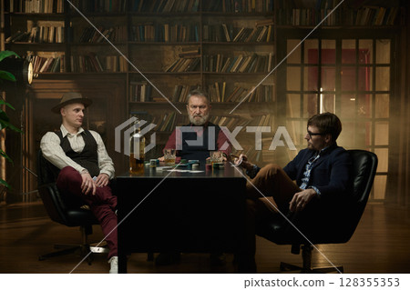 Three distinguished gentlemen playing poker game in a vintage old library 128355353