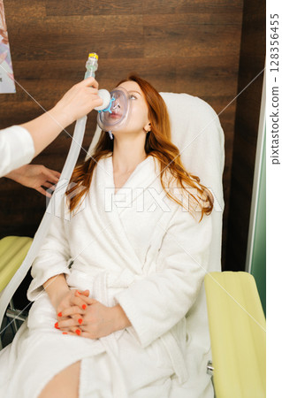 Vertical shot of medical professional supporting patient to using oxygen mask for respiratory therapy during clinical rehabilitation procedure. Training increases body adaptation abilities, close-up. Vertical shot of medical professional supporting patient to using oxygen mask for respiratory therapy during clinical rehabilitation procedure. Training increases body adaptation abilities, close-up. 128356455