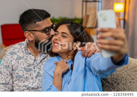 Indian family couple man woman taking selfie on smartphone with kiss on cheek, romantic fun moment 128356495