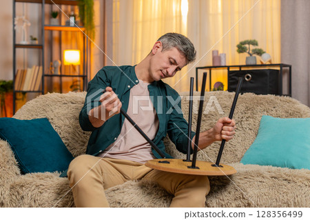 Young man fixes wooden table at home with confident hands calm focused expression enjoying handywork 128356499