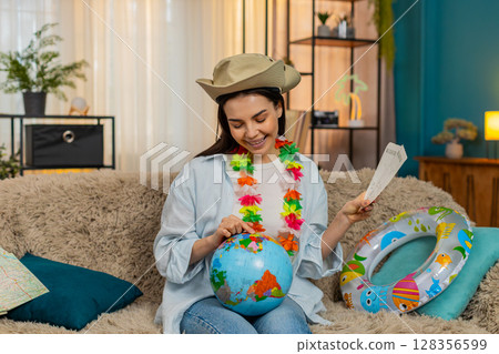 Happy woman on sofa with swim ring holding globe and plane tickets planning exciting future trip 128356599