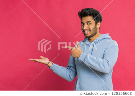 Young man showing thumbs up and pointing at left on blank space place for your advertisement logo 128356608