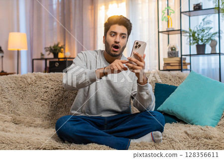 Happy man using smartphone scrolls through news on smartphone reacting with surprise and excitement 128356611