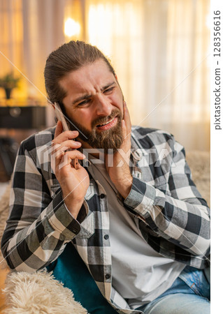 Young man toothache at home, phone call, pain, cheek press, urgent dentist clinic, irritated face 128356616