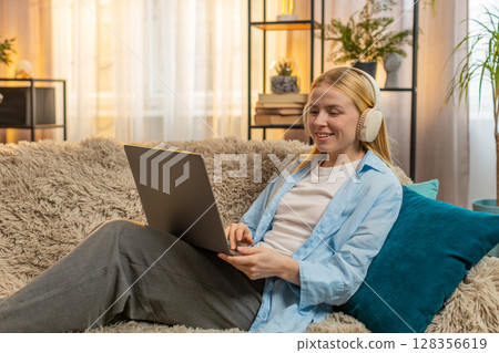 Young woman freelancer relaxed on couch, laptop work, cozy home comfort, sunset vibe, creative flow 128356619