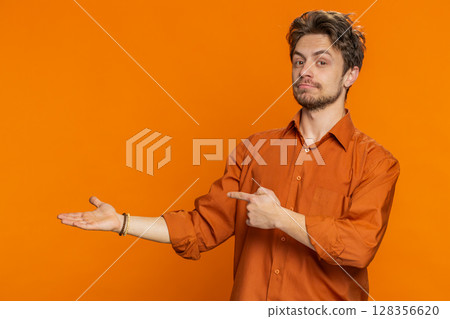 Young man showing thumbs up and pointing at left on blank space place for your advertisement logo 128356620