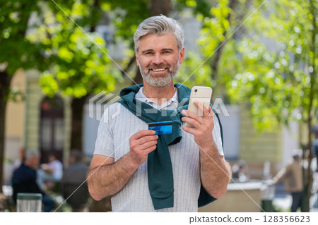 Happy mature man use credit bank card smartphone while transferring money purchases online shopping Happy mature man use credit bank card smartphone while transferring money purchases online shopping 128356623