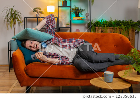 Irritated angry man covers ears with cushions annoyed by noisy loud music neighbors repair work Irritated angry man covers ears with cushions annoyed by noisy loud music neighbors repair work 128356635